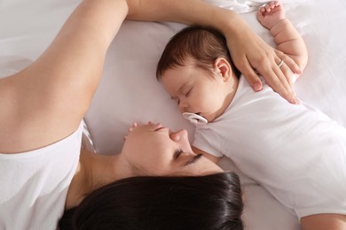 Photo of Young mother resting near her sleeping baby on bed, top view