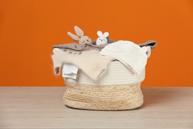 Photo of Laundry basket with baby clothes and crochet toys on wooden table against orange background