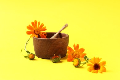 Photo of Mortar with pestle and beautiful calendula flowers on yellow background