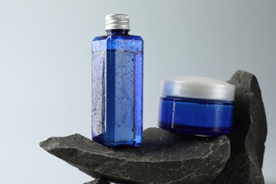 Photo of Bottle and jar of cosmetic products on stones against light grey background