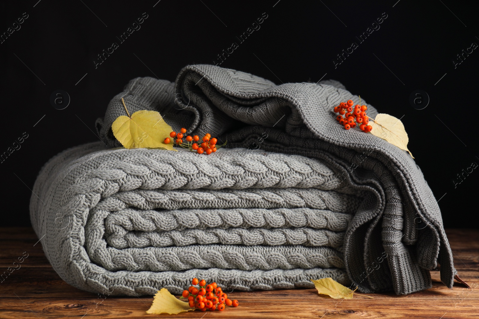 Photo of Knitted plaids with red berries and dry leaves on wooden table