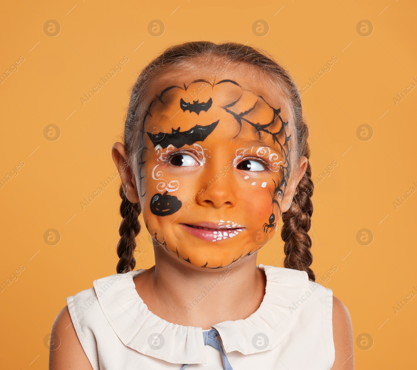 Photo of Cute little girl with face painting on orange background