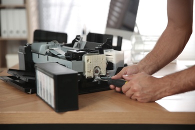 Photo of Repairman with screwdriver fixing modern printer indoors, closeup