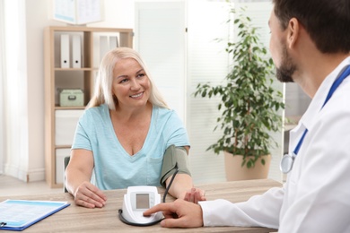 Photo of Doctor checking mature woman's pulse with medical device in hospital