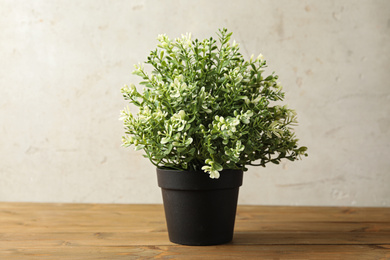 Artificial plant in dark flower pot on wooden table