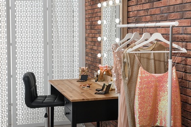 Hangers with stylish clothes on rack in makeup room