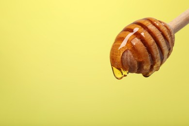 Photo of Delicious honey flowing down from dipper against yellow background, closeup. Space for text