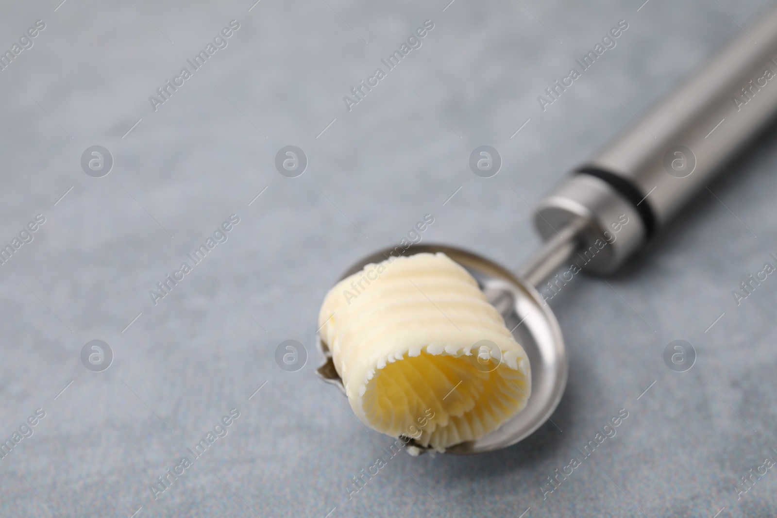 Photo of Tasty butter curl in spoon on light grey table, closeup. Space for text