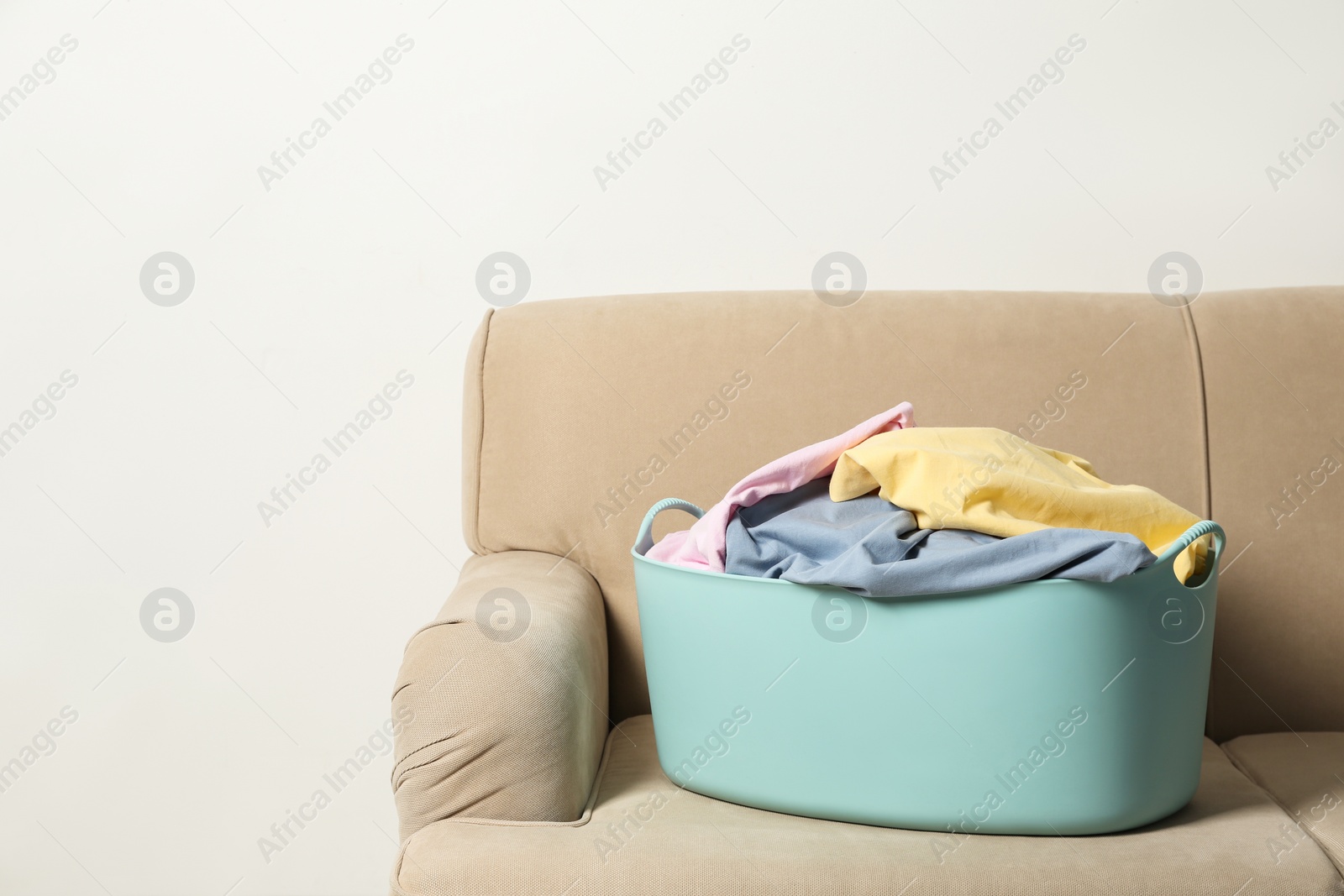 Photo of Laundry basket with dirty clothes on sofa against light background. Space for text