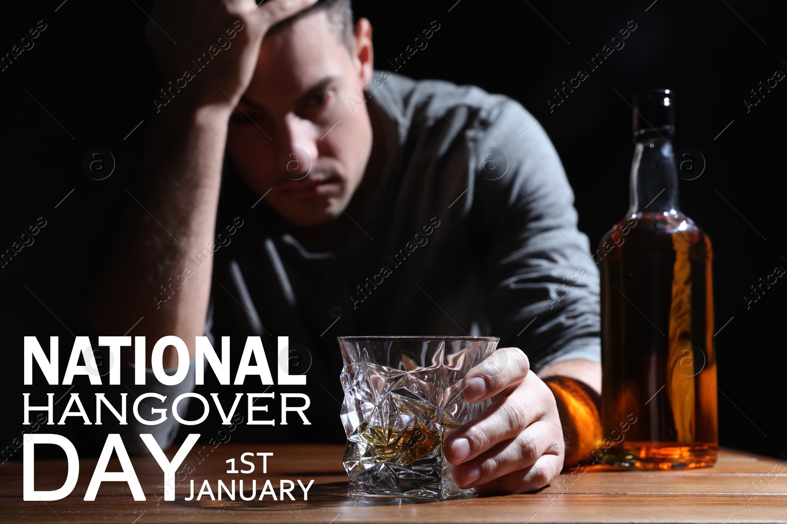 Image of National hangover day - January 1st. Man holding glass of alcoholic drink at table against black background