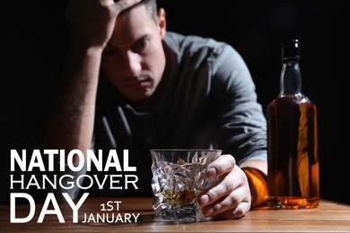 National hangover day - January 1st. Man holding glass of alcoholic drink at table against black background