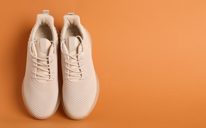 Pair of stylish sport shoes on orange background, top view. Space for text