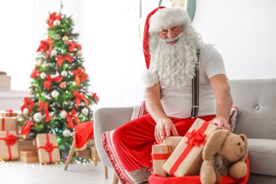Authentic Santa Claus packing gifts into bag indoors