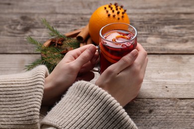 Woman with glass cup of aromatic mulled wine at wooden table, closeup