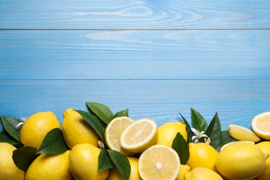 Photo of Many fresh ripe lemons with green leaves and flowers on blue wooden table, flat lay. Space for text
