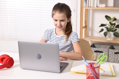 Photo of E-learning. Cute girl using laptop during online lesson at table indoors