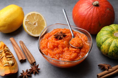 Photo of Bowl of delicious pumpkin jam and ingredients on grey table