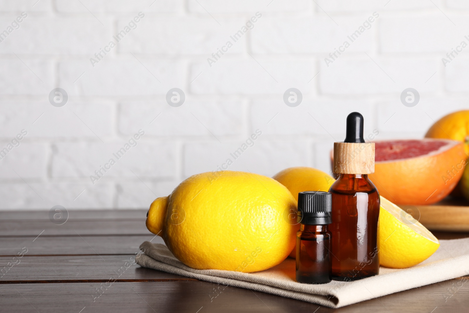 Photo of Bottles of essential oils with different citrus fruits on wooden table against white brick wall. Space for text