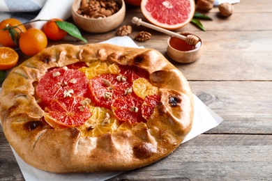 Delicious galette with citrus fruits and walnuts on wooden table, closeup