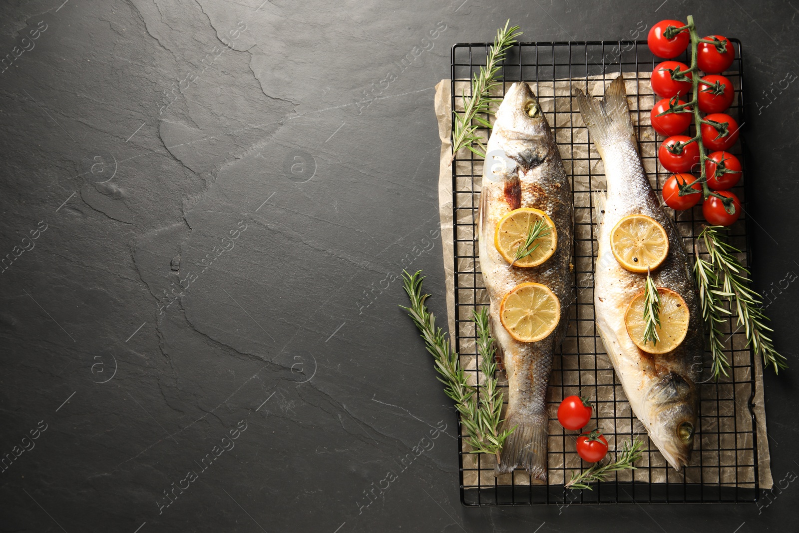 Photo of Baked fish with tomatoes, rosemary and lemon on black textured table, top view. Space for text