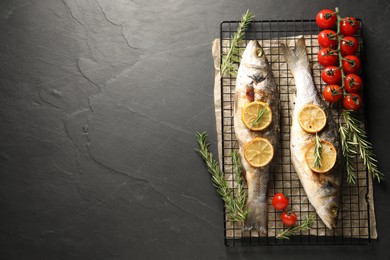 Photo of Baked fish with tomatoes, rosemary and lemon on black textured table, top view. Space for text