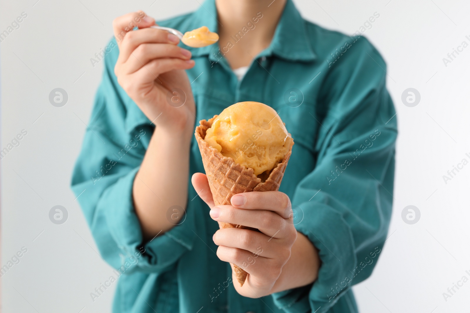 Photo of Woman eating yellow ice cream in wafer cone on light background, closeup