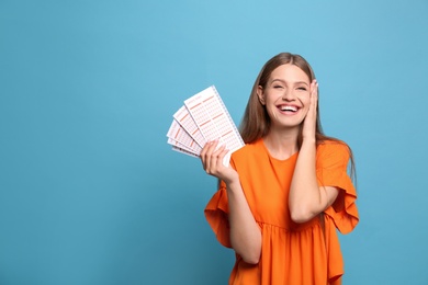 Photo of Portrait of happy young woman with lottery tickets on light blue background, space for text