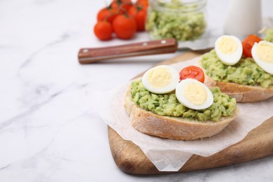 Photo of Delicious sandwiches with guacamole, eggs and tomatoes on white marble table, space for text