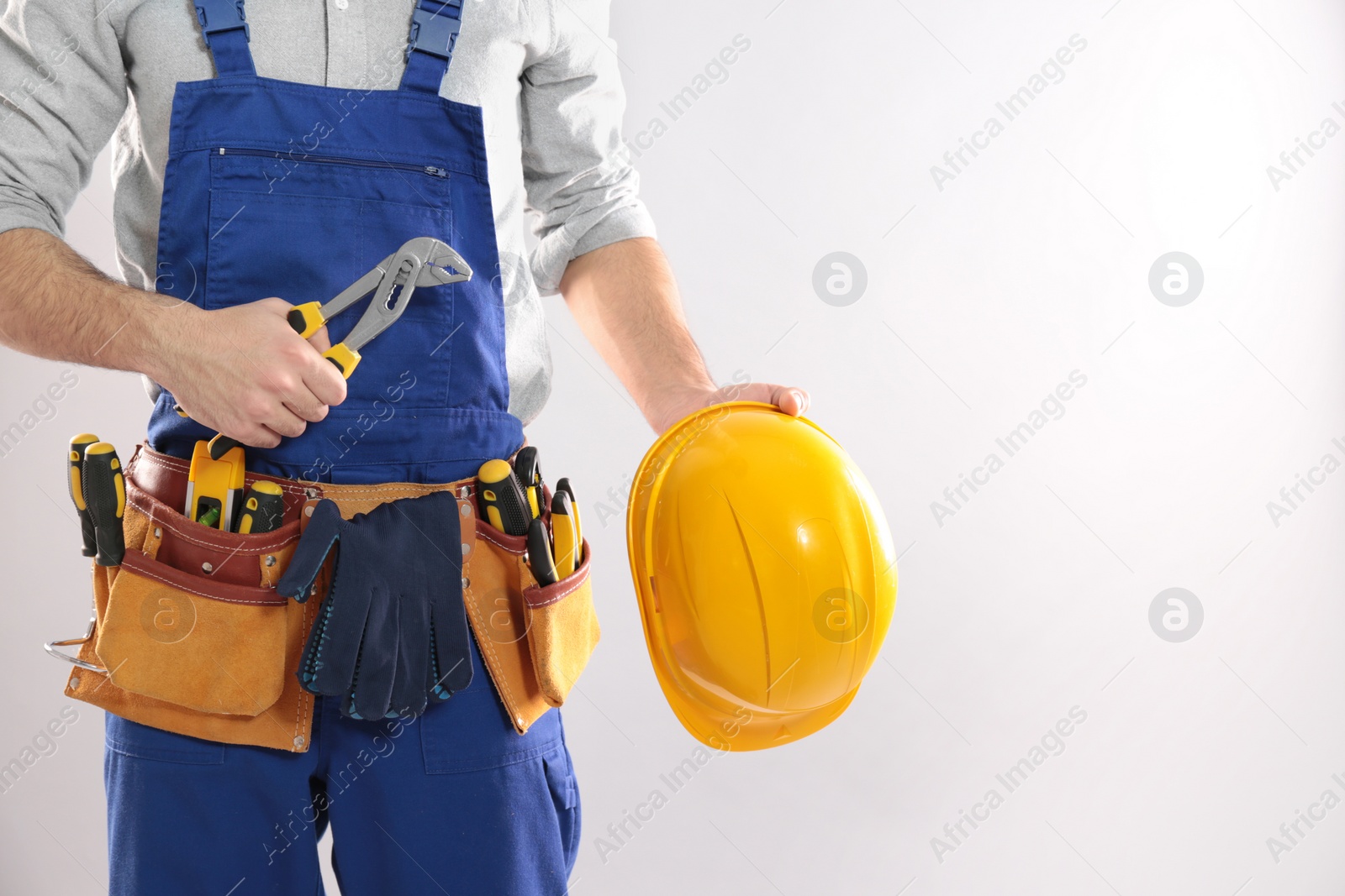 Photo of Construction worker with instrument, hard hat and tool belt on light background, closeup. Space for text