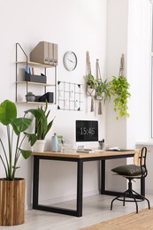 Cozy workplace with computer, modern furniture and houseplants at home