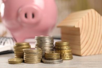 House model, piggy bank and stacked coins on wooden table, selective focus