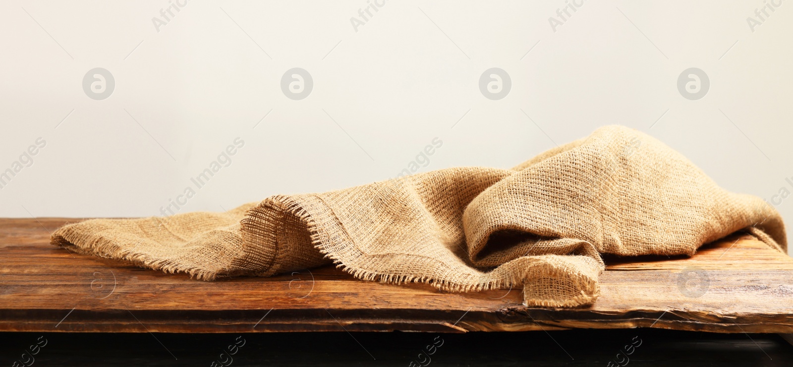 Photo of Natural burlap fabric on wooden table against light background. Space for text