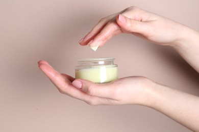 Woman with jar of cream on beige background, closeup