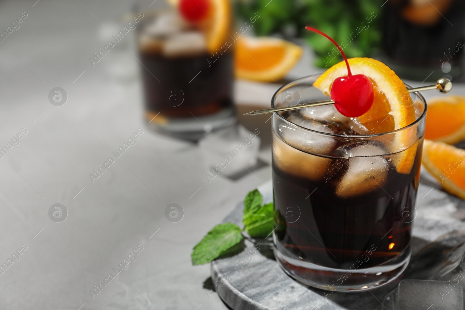 Photo of Glass of delicious cocktail decorated with cherry and orange on light grey table, closeup. Space for text