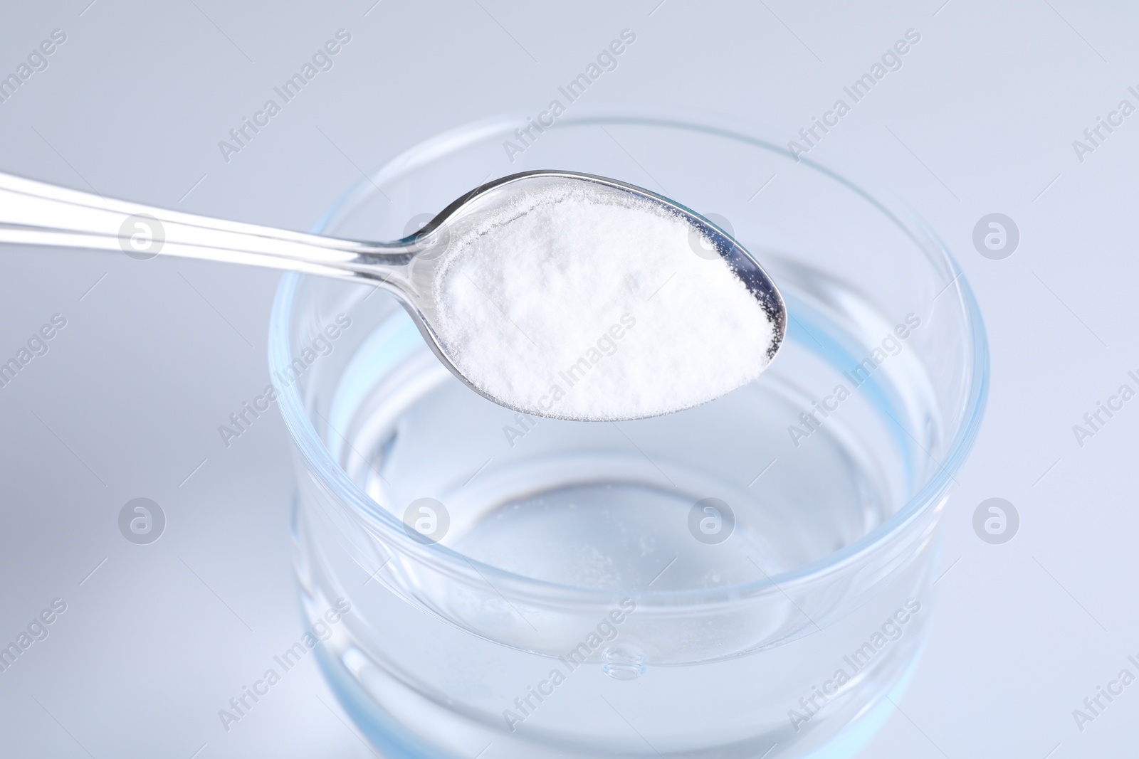 Photo of Adding baking soda into glass of water on light background, closeup