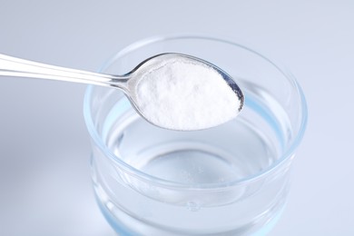 Photo of Adding baking soda into glass of water on light background, closeup