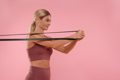 Woman exercising with elastic resistance band on pink background. Space for text