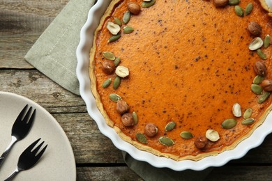 Photo of Delicious pumpkin pie with seeds and hazelnuts served on wooden table, flat lay