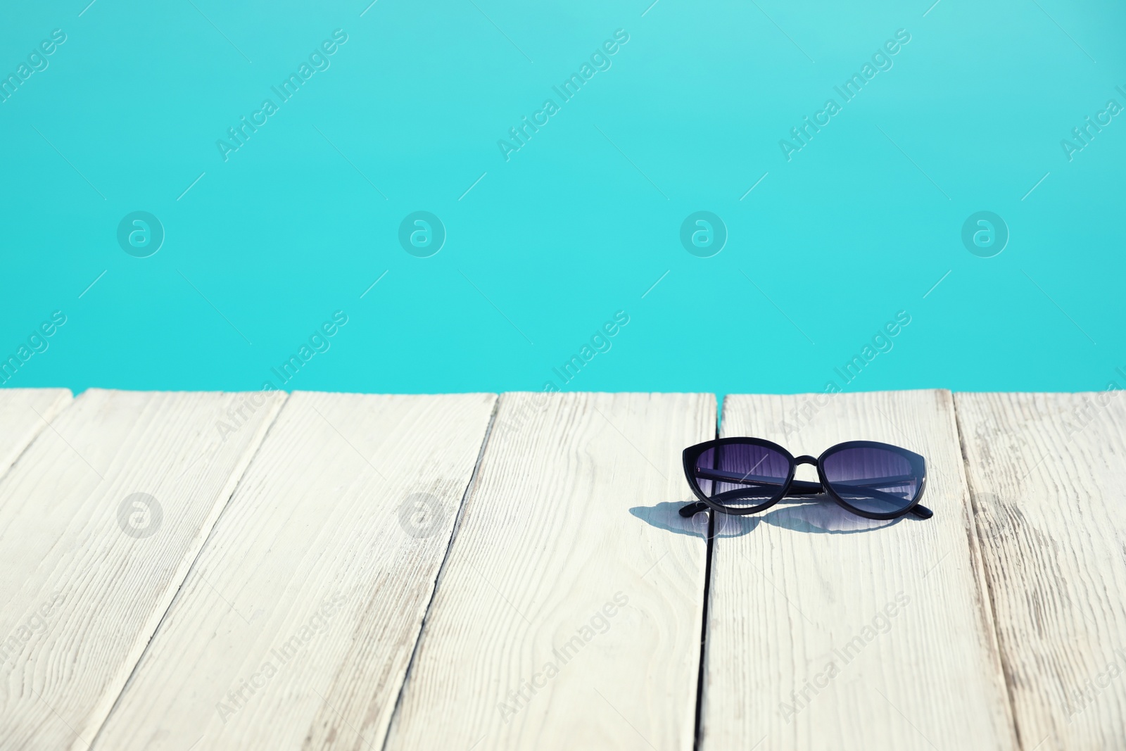 Photo of Sunglasses near swimming pool on sunny day. Space for text