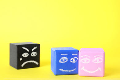 Photo of Cubes with drawn faces on yellow background, space for text. Concept of jealousy