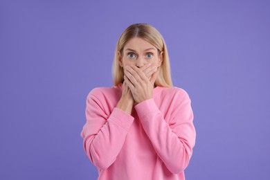 Portrait of embarrassed woman covering mouth with hands on purple background