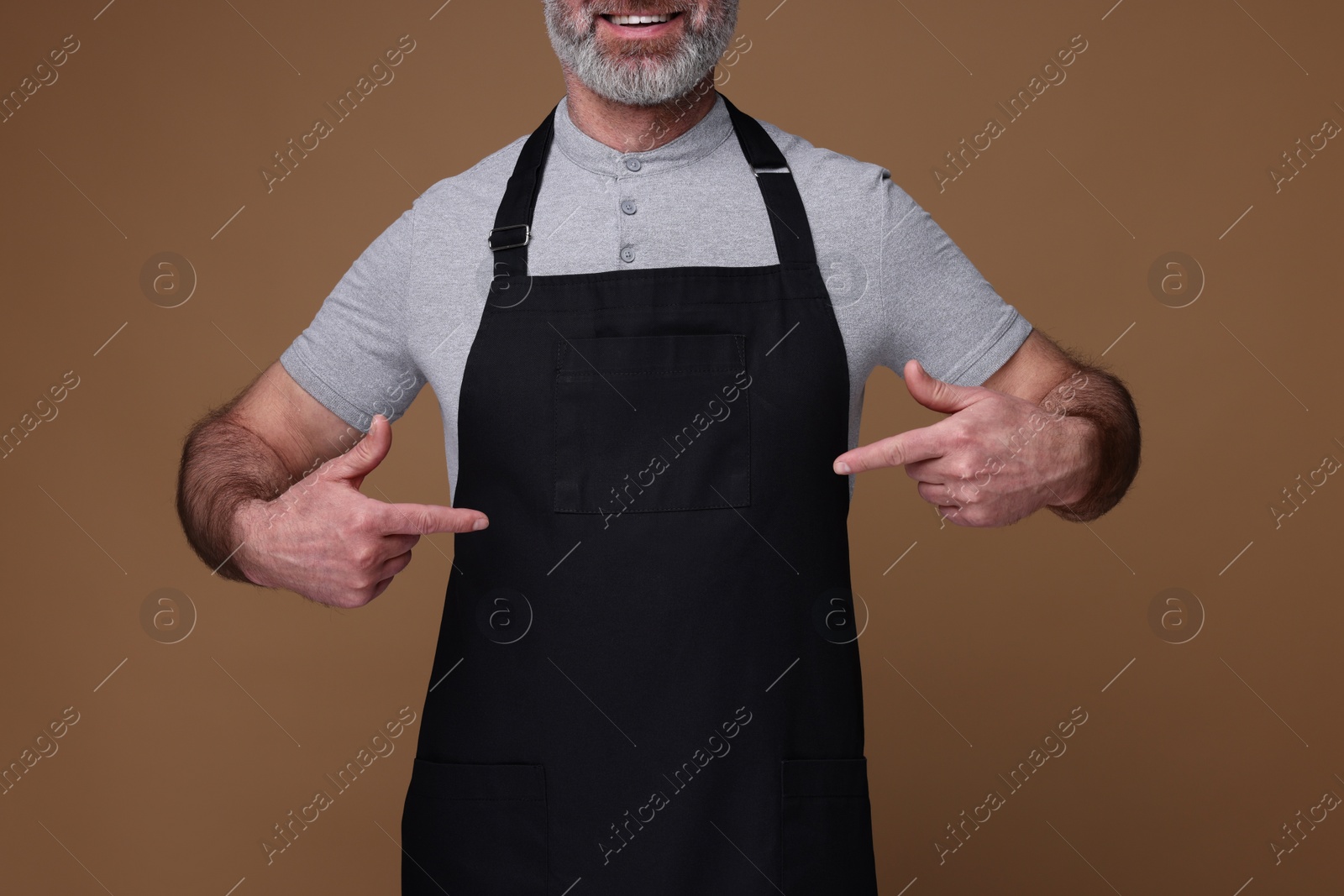 Photo of Man pointing at kitchen apron on brown background, closeup. Mockup for design