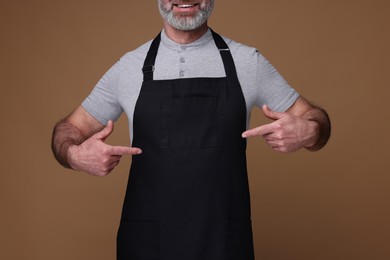 Photo of Man pointing at kitchen apron on brown background, closeup. Mockup for design