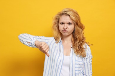 Dissatisfied young woman showing thumb down gesture on yellow background