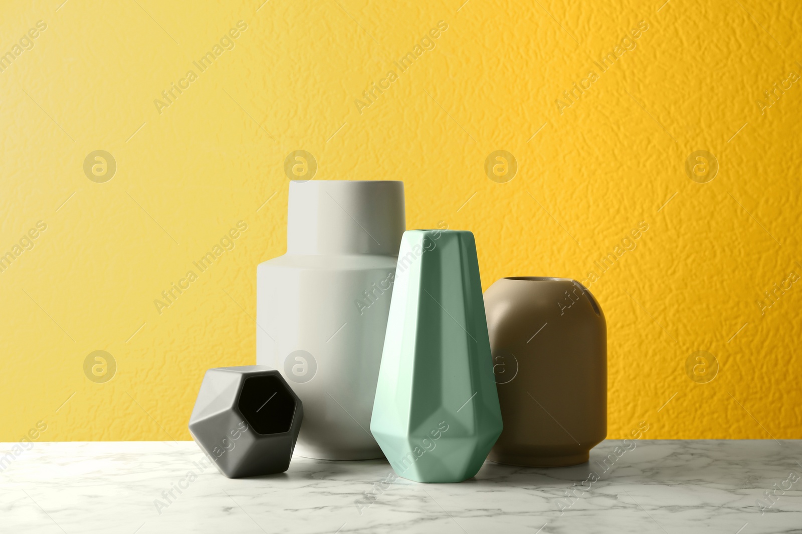 Photo of Stylish ceramic vases on white marble table against yellow background