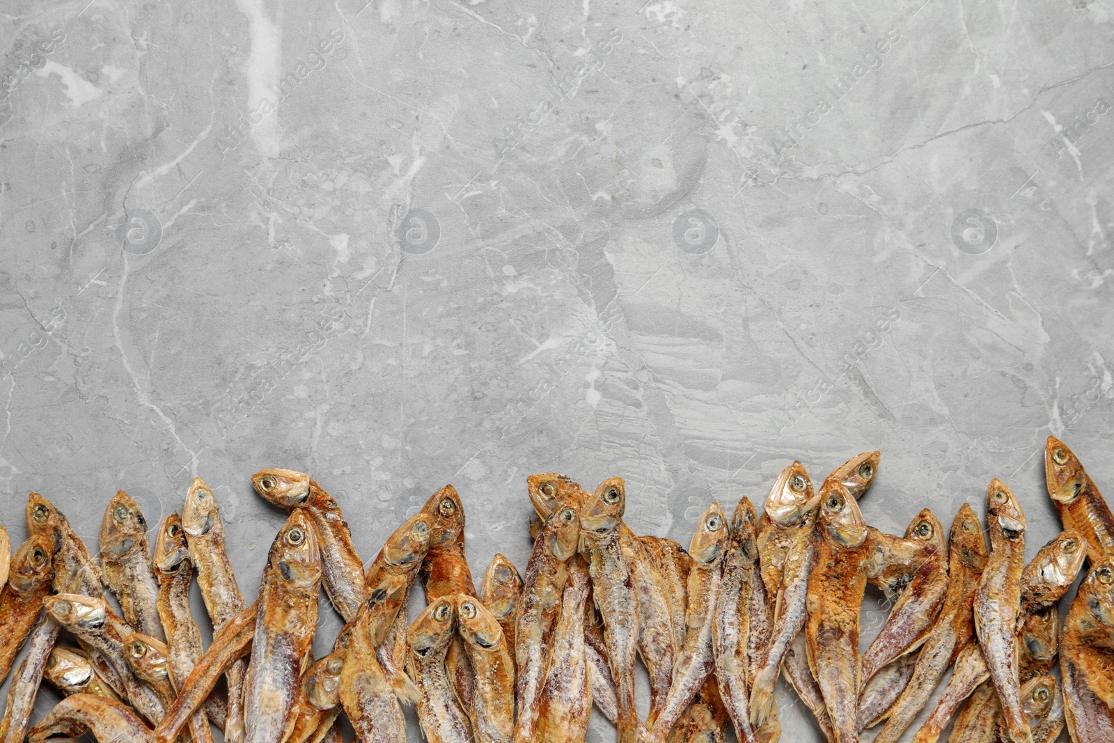 Photo of Tasty dried anchovies on light grey marble table, flat lay. Space for text