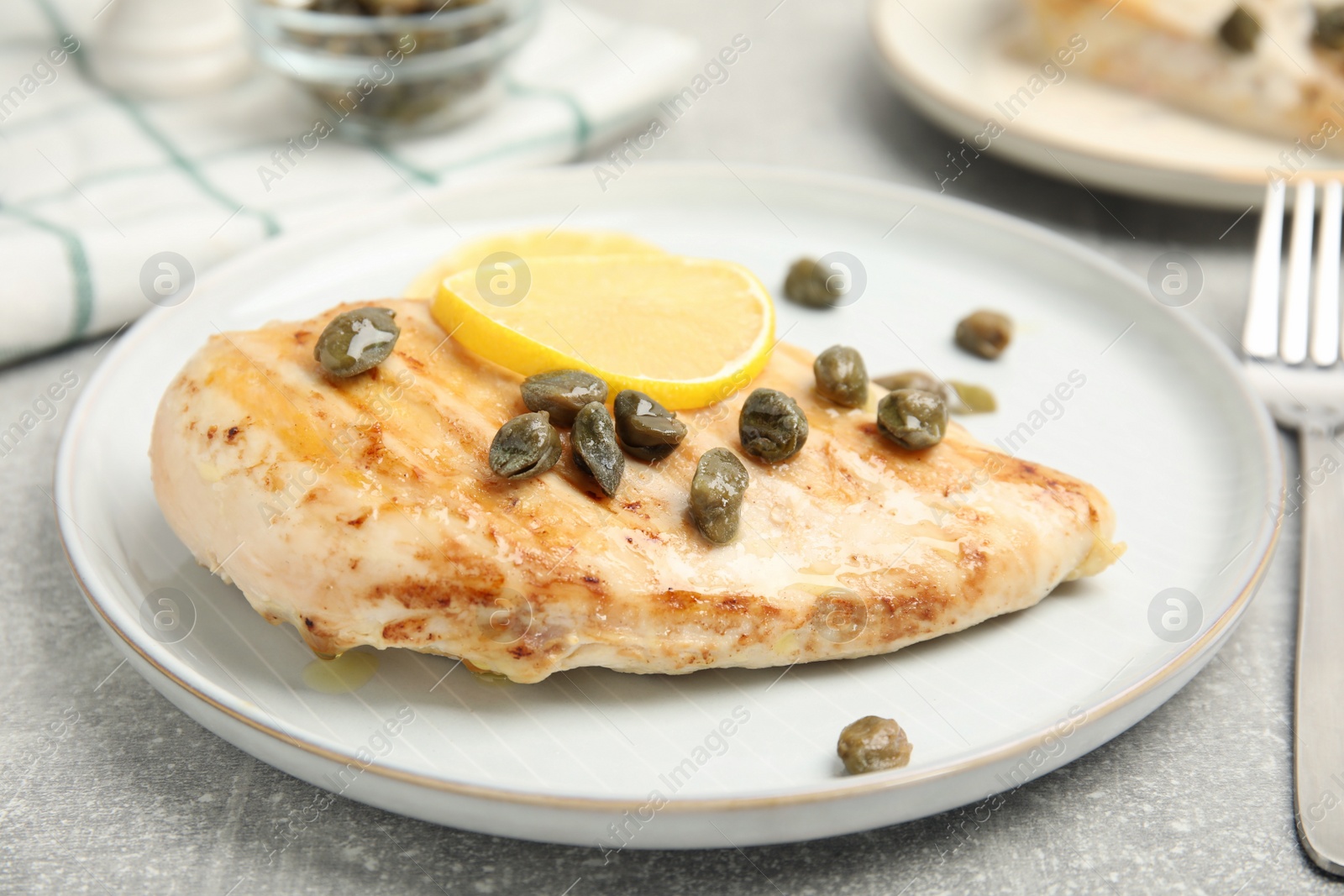 Photo of Delicious chicken fillet with capers and lemon served on light grey table, closeup