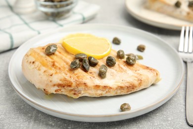 Photo of Delicious chicken fillet with capers and lemon served on light grey table, closeup