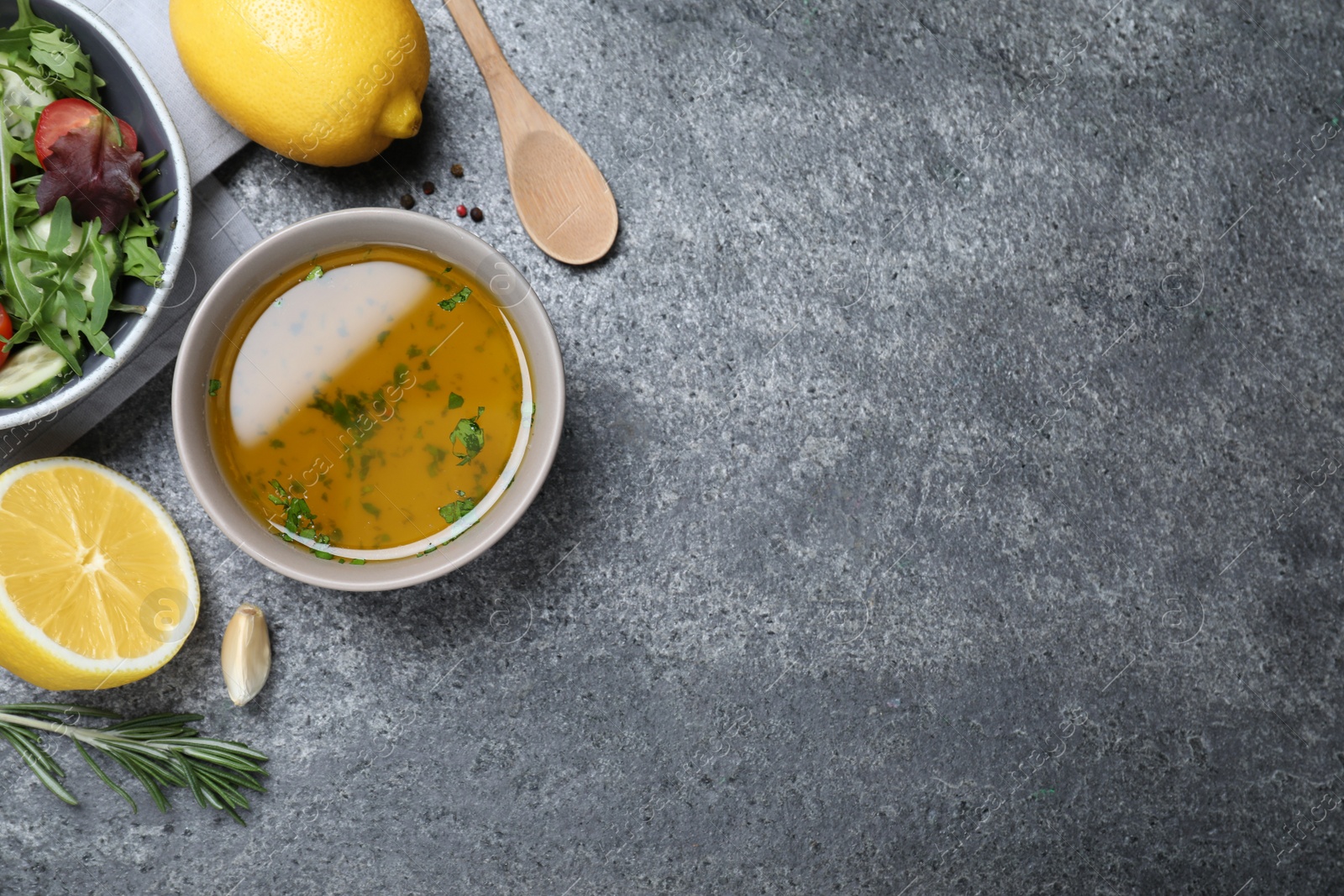 Photo of Bowl with lemon dressing near salad on grey table, flat lay with space for text. Delicious salad dressing