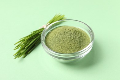 Photo of Wheat grass powder in bowl and fresh sprouts on green table